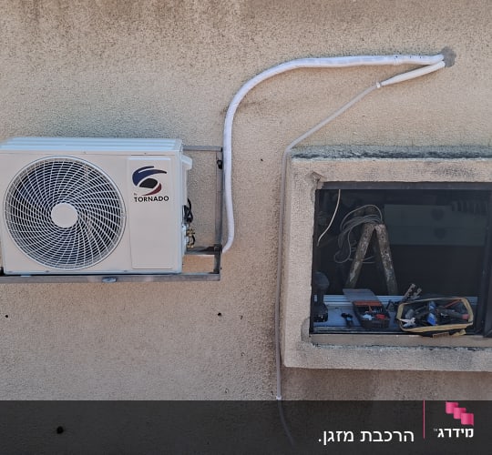 יחידת מזגן מותקנת על קיר חיצוני עם כלים בחלון